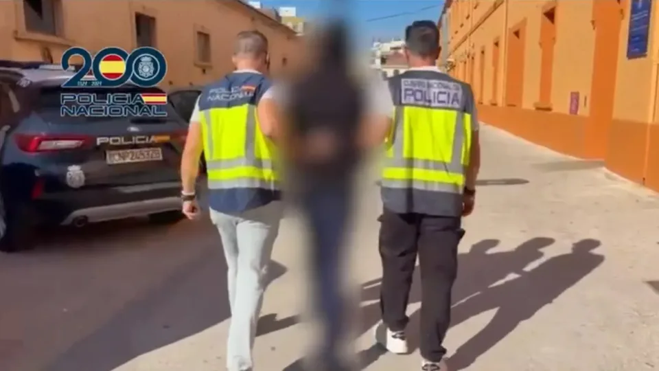 Dos agentes de la Policía Nacional acompañan a un detenido con la figura desenfocada; fotograma de la detención relacionada con Blocus Vlc difundido por la Policía el 29 de octubre de 2026