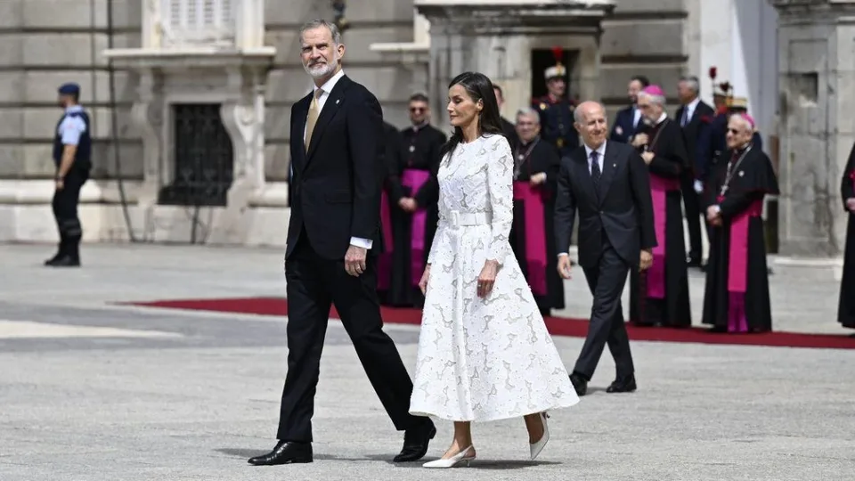 Felipe VI y Letizia caminan juntos durante un acto oficial con representantes eclesiásticos al fondo.