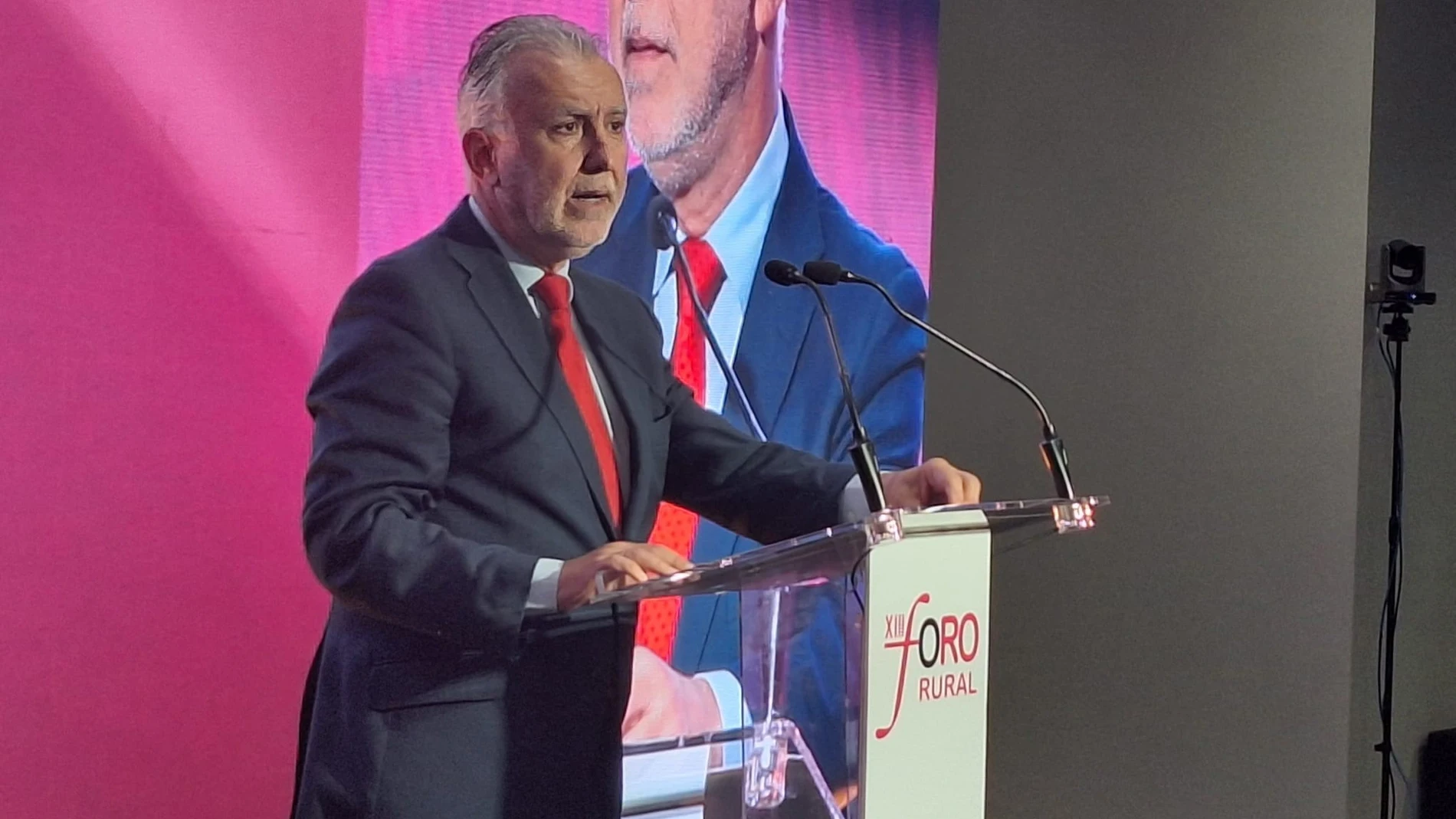 Un ponente con traje oscuro y corbata roja interviene ante un atril en un acto identificado como Foro Rural.