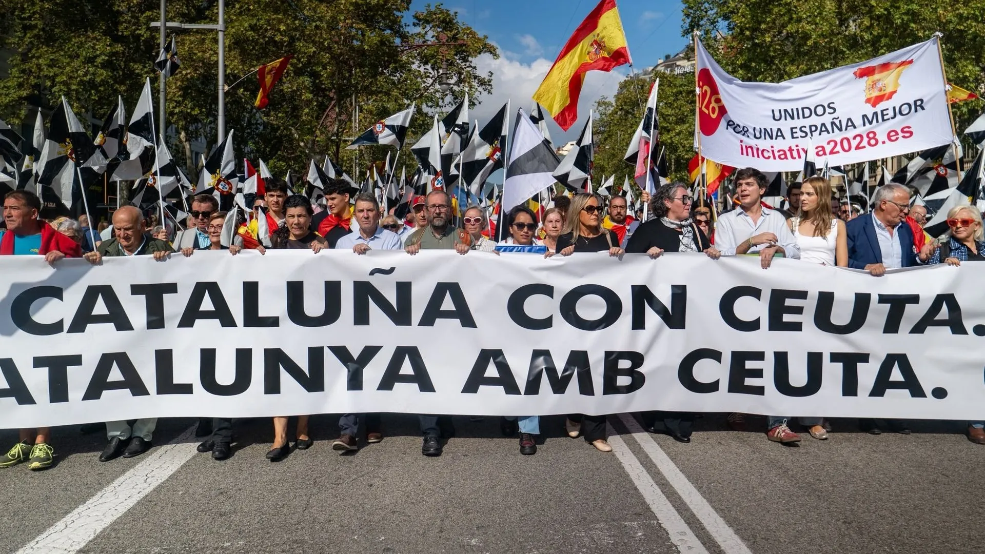 Manifestantes avanzan por una avenida con una gran pancarta bilingüe «Cataluña con Ceuta. Catalunya amb Ceuta» y banderas españolas.